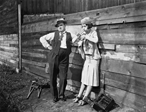 Drab: Woman practicing her trumpet while a man is standing