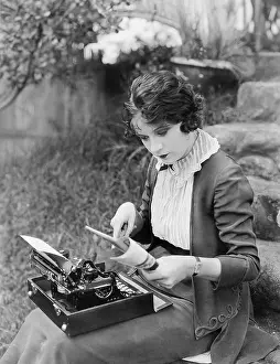 Employ: Woman sitting in the yard with a typewriter on her lap