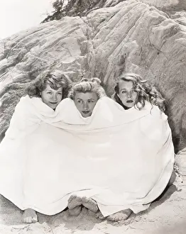Huddled: Three women huddled under a towel on beach