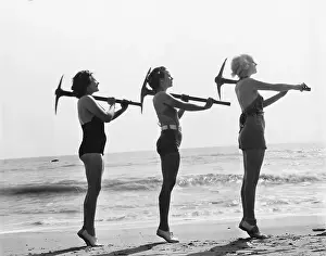 Conformity: Three women posing with a pick ax on the beach