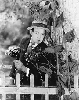 Distraught: Young man hiding behind a tree with a bouquet of
