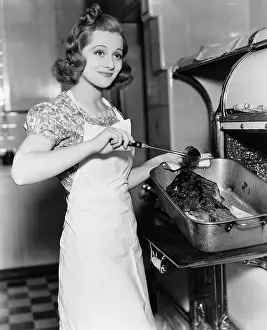 Domestication: Young woman basting a goose in the kitchen