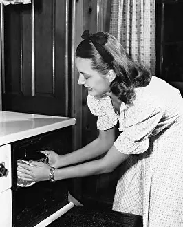 Convenient: Young woman in her kitchen pulling a pot out of the oven