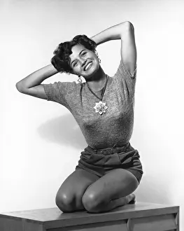 Young woman kneeling on a table with hands behind her head