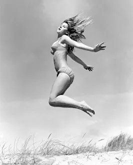 Ecstatic: Young woman leaps up from a sand dune, Cornwall