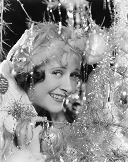 Tinsel: Young woman looking through the branches of a Christmas