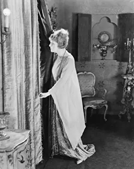 Peaking: Young woman looking out from behind her curtains