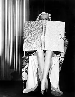 Peaking: Young woman looking over top of an oversized book