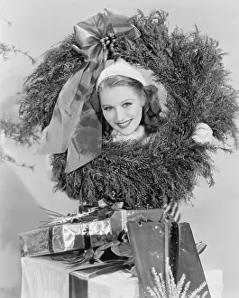 X Mas: Young woman looking through a wreath with presents