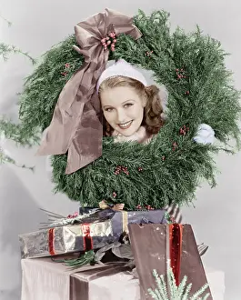 X Mas: Young woman looking through a wreath with presents