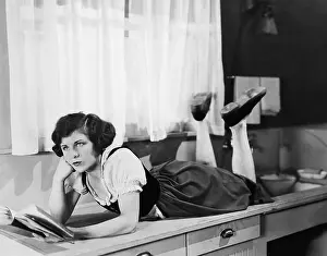 Ponder: Young woman lying on a kitchen counter holding a