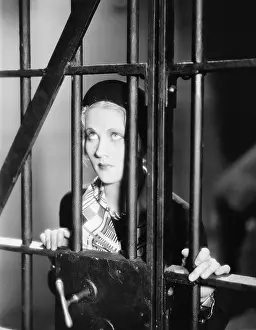 Lamenting: Young woman standing behind bars in a prison cell