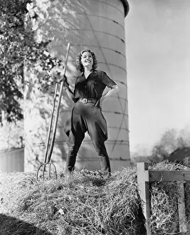 Employ: Young woman standing on a haystack and holding a pitchfork